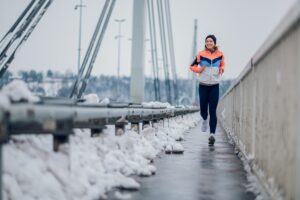 Kobieta biegnąca zimą po zaśnieżonym moście, aktywność fizyczna jako walka z zimowym zmęczeniem